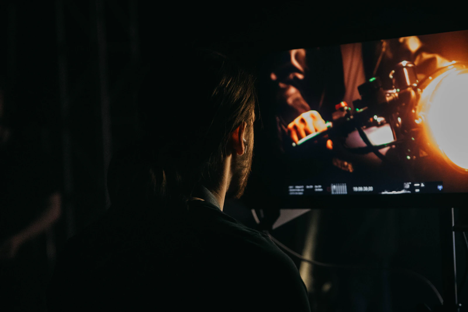 Viewer seen from behind in a dark room watching a dim, high-contrast scene on a screen