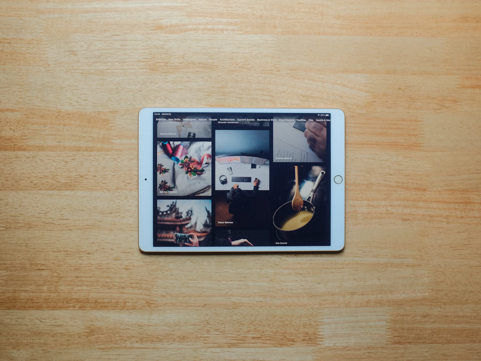 Older white tablet with a home button lying on a wooden table, its screen showing a grid of image and video thumbnails
